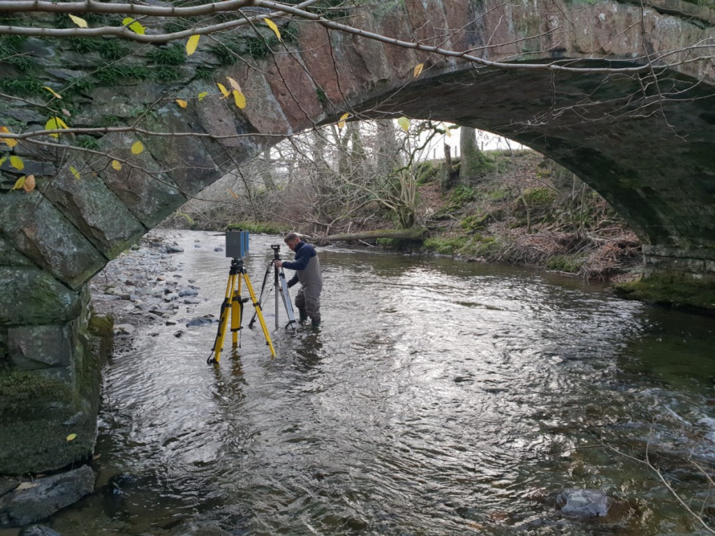 3D scanner and surveyor adjusting a tripod in the water under a bridge
