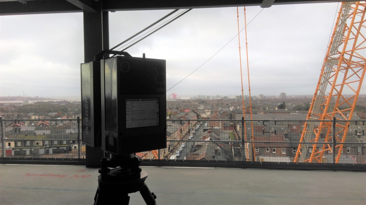 3D scanner on a concrete slab inside a building under construction with a crane and cityscape in the background