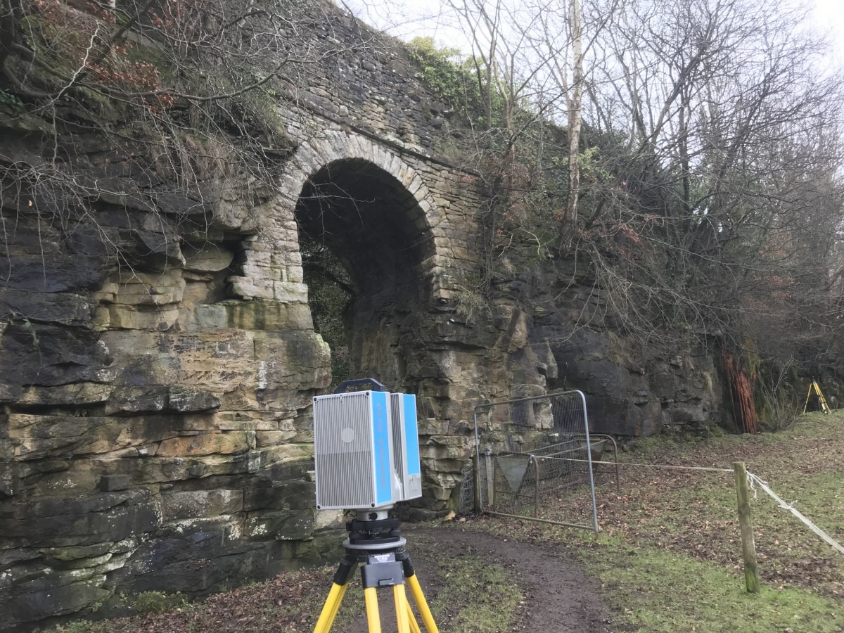 Blue 3D Scanner on Yellow Tripod in front of a stone archway through a quarry entrance.