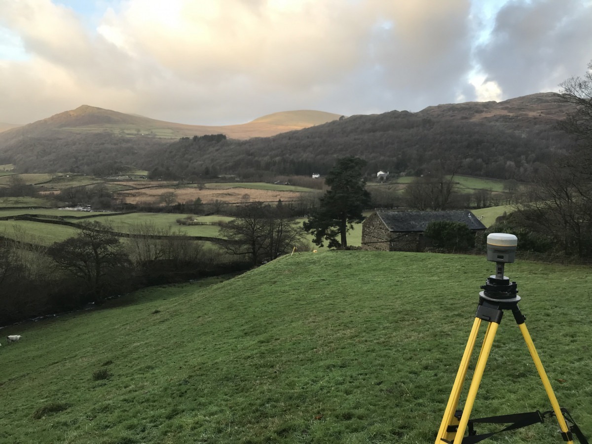GNSS Receiver on Yellow tripod in field with a valley and rolling hills in the background.