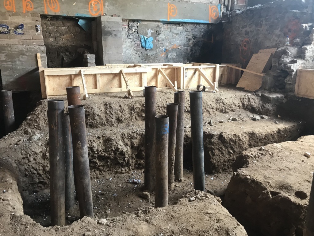 Steel tube piles protruding from the ground within a foundation excavation.