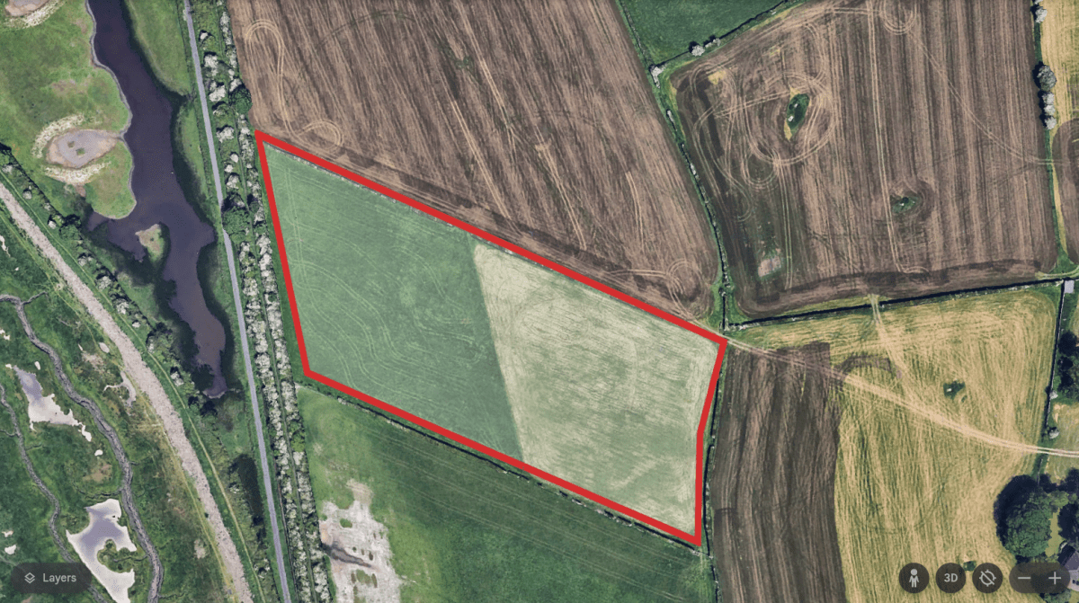 Aerial view of fields and a body of water. One field is outlined in red.